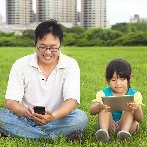 Father and daughter using mobiles in the park