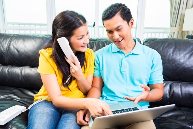 Couple sitting on lounge using a phone and laptop