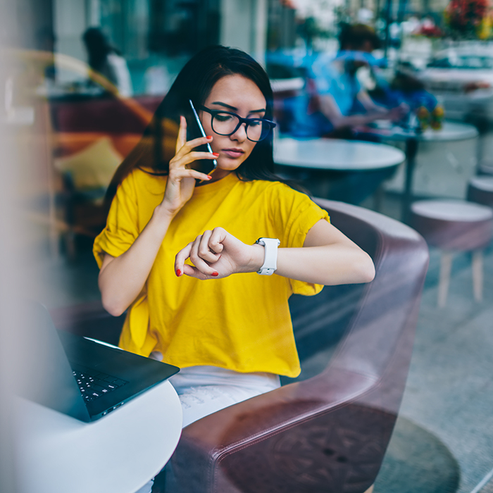 Young woman in yellow shirt on smart phone looks at watch 