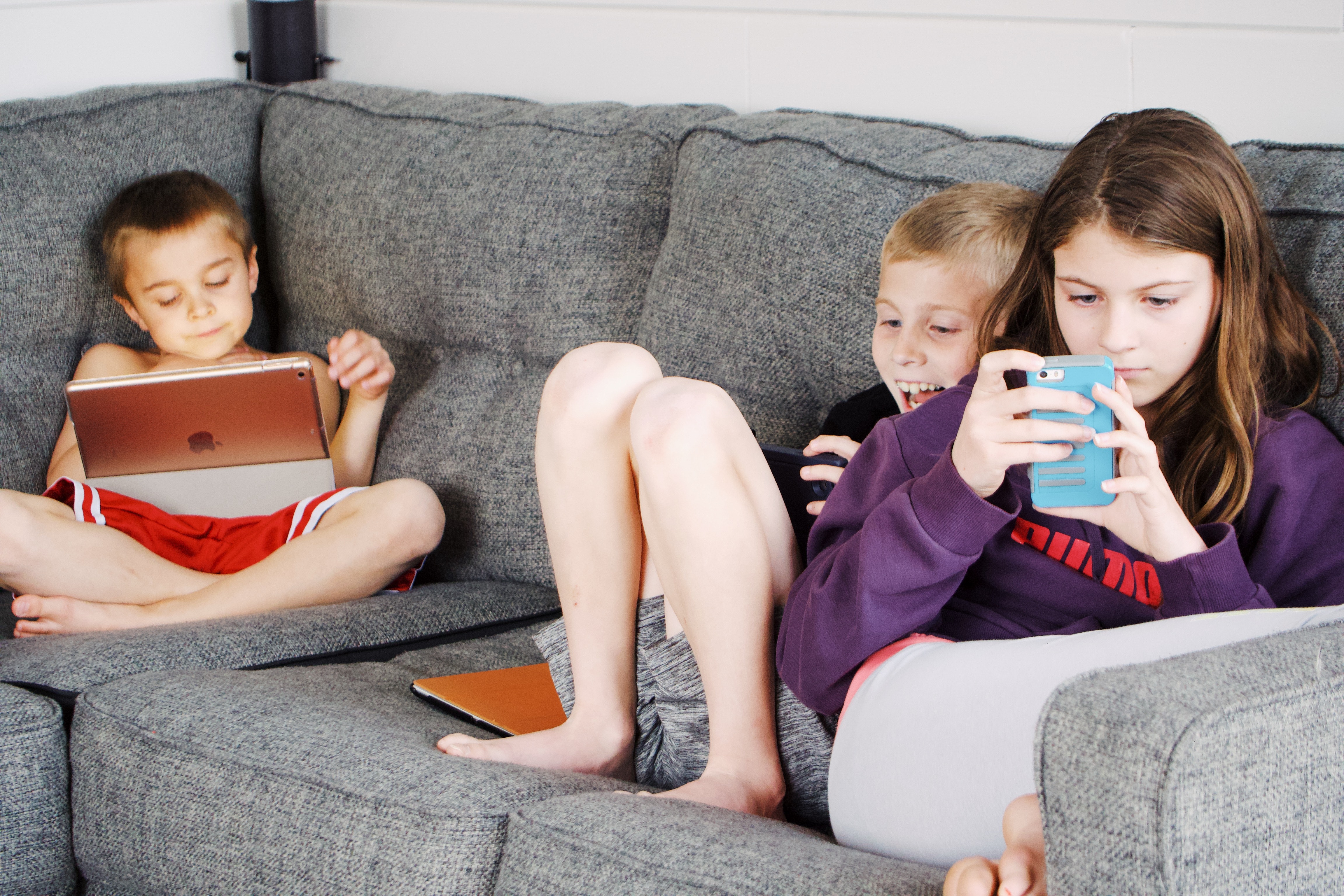 Image shows three children using various devices, including an iPad and a smart phone