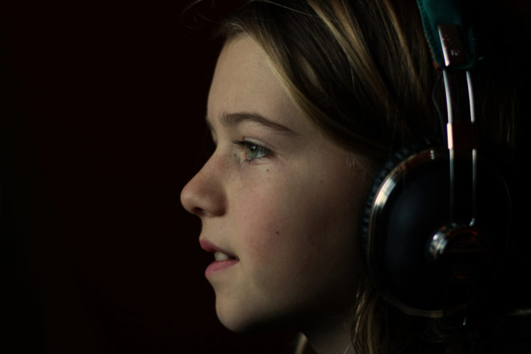 young girl wearing headphones looks to right against black background
