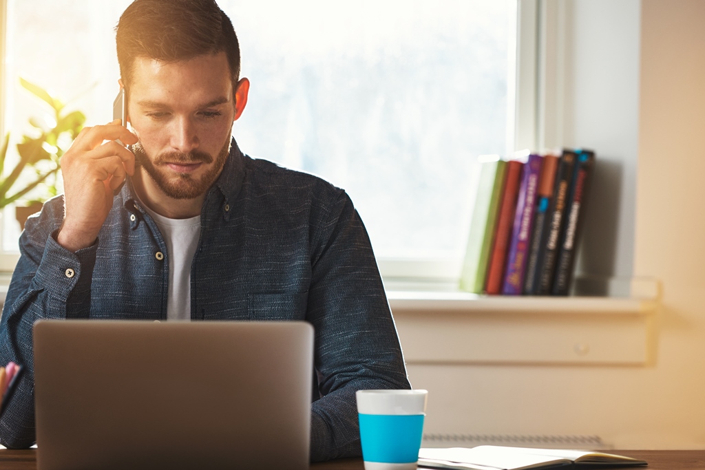 Young man talking on his phone at the computer