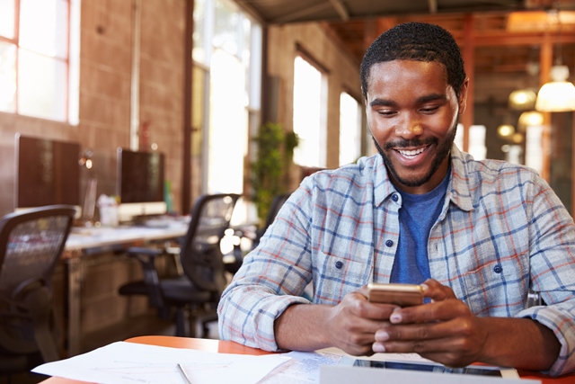 Young man sitting at desk looking at smartphone