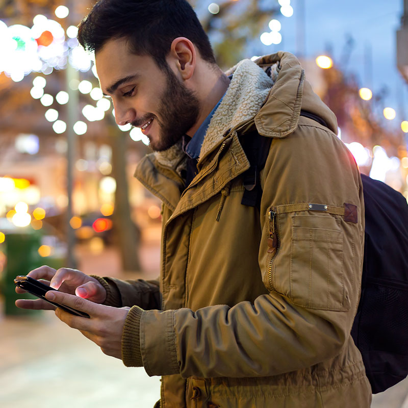 Man with backpack on street smiling at phone