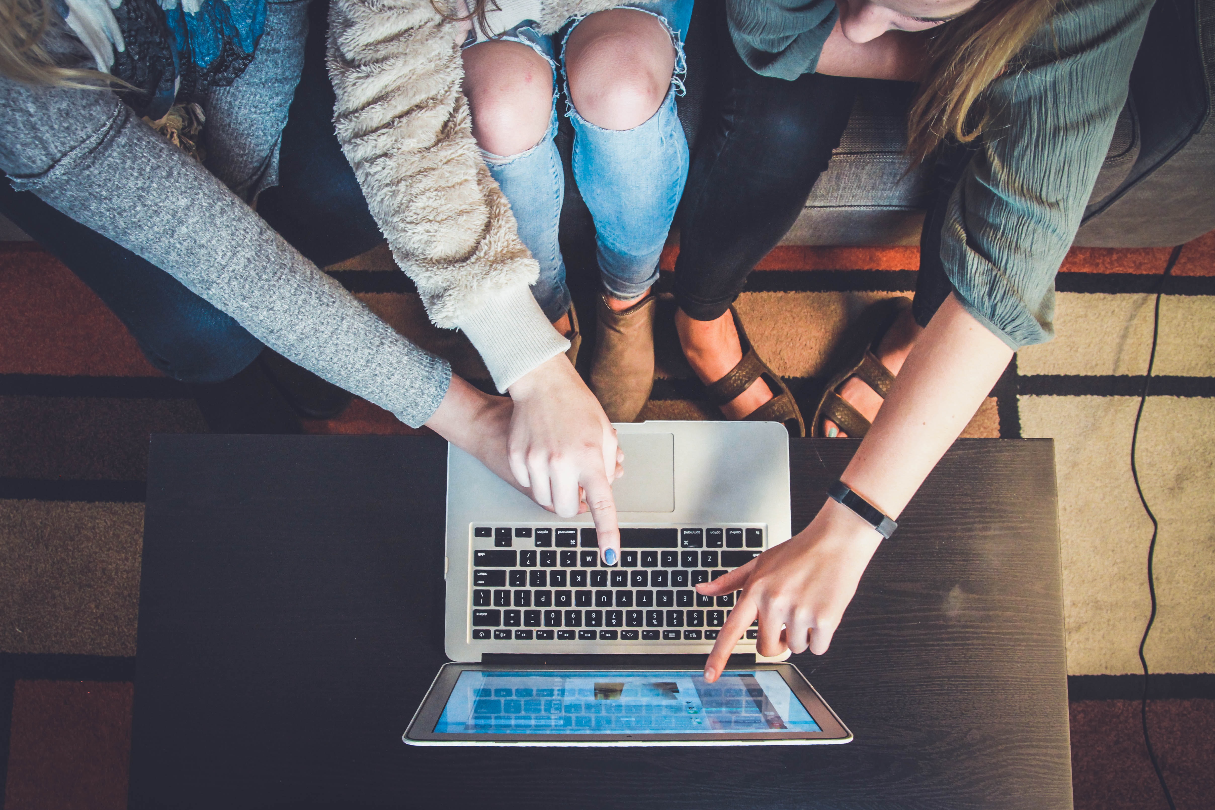 Image description: three people sit on a lounge, looking at a laptop computer