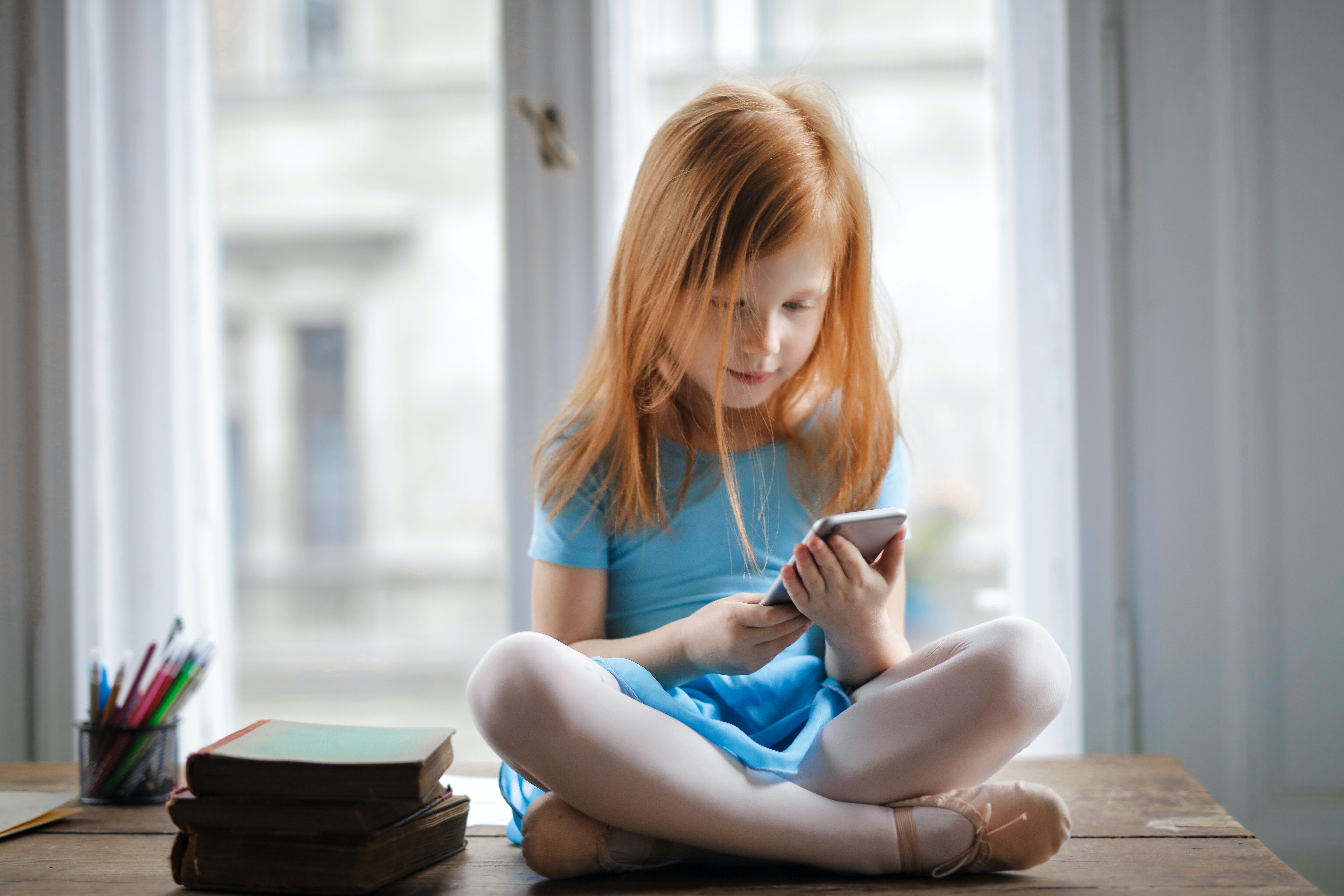 A young girl sitting on the floor, using an iPhone. 