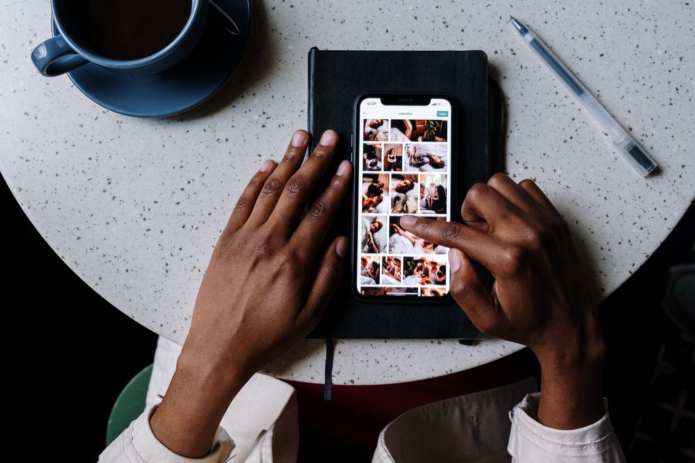 Someone is scrolling through photos on an Apple iPhone, placed on a table next to a cup of coffee